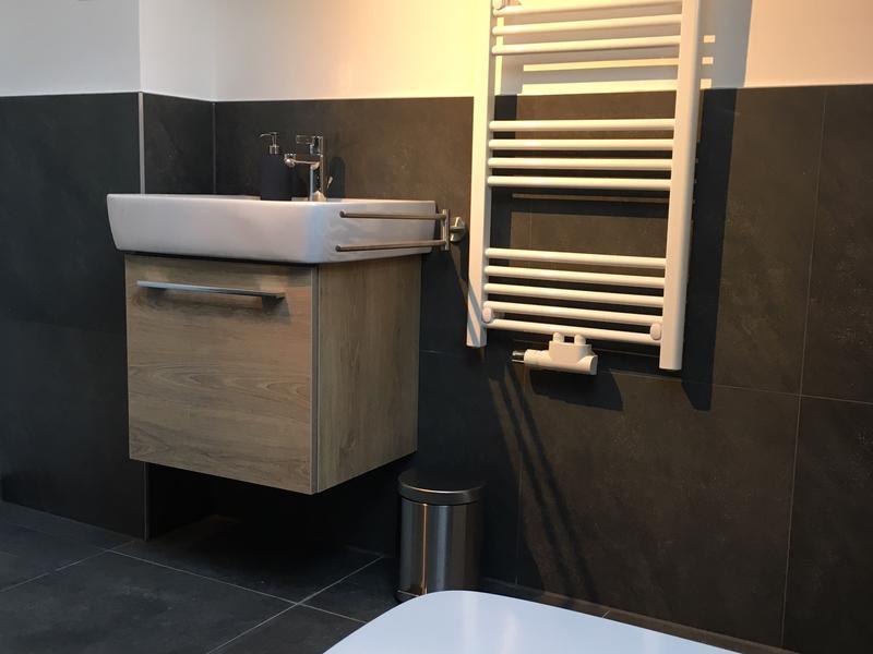 Ein modernes Bad mit dunklen Fliesen, weißem Waschbecken und Handtuchhalter